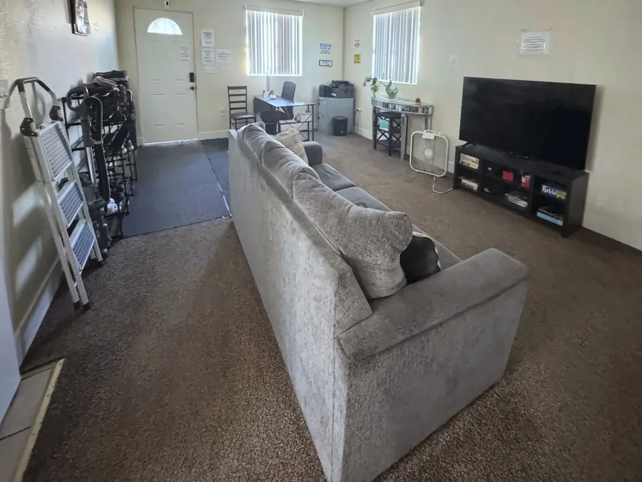 Common room at the East 69th Street house with a grey sofa a television and a desk