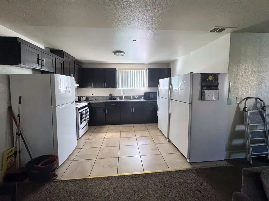 Shared kitchen at the East 69th Street house with dark cabinets a gas range and three refrigerators